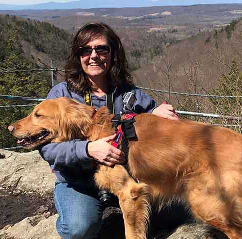 Kathleen Hesketh, freelance writer with golden retriever on mountain ledge.